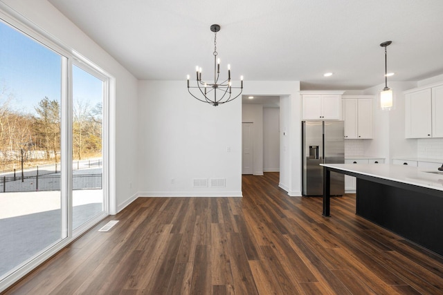 kitchen with stainless steel fridge, decorative backsplash, white cabinetry, an inviting chandelier, and decorative light fixtures