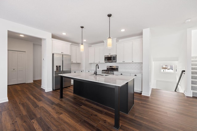 kitchen with a center island with sink, appliances with stainless steel finishes, pendant lighting, sink, and white cabinetry