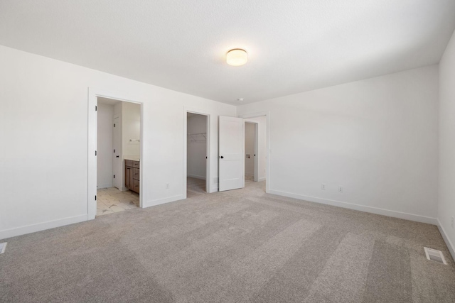 unfurnished bedroom featuring ensuite bathroom, a closet, light carpet, and a spacious closet