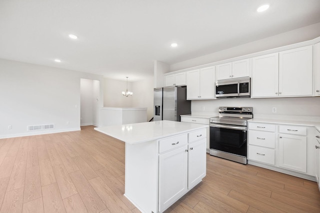 kitchen with appliances with stainless steel finishes, light hardwood / wood-style floors, white cabinetry, and a kitchen island