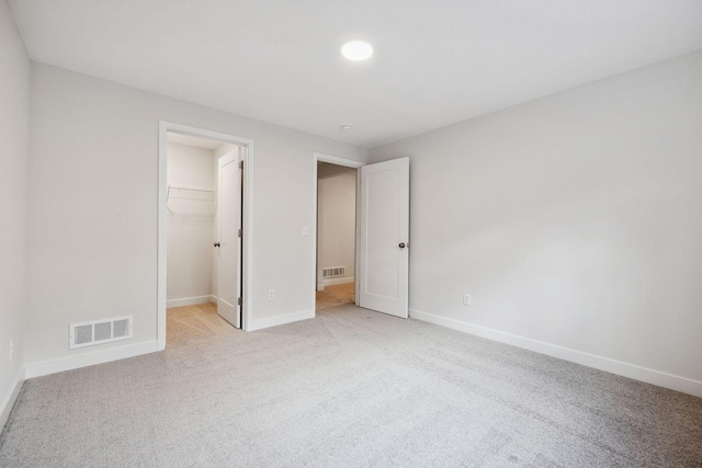 unfurnished bedroom with a walk in closet, a closet, and light colored carpet