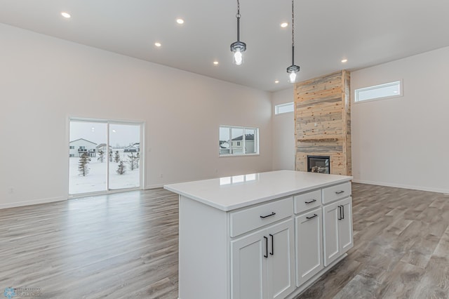 kitchen featuring pendant lighting, a kitchen island, white cabinetry, light hardwood / wood-style floors, and a tiled fireplace