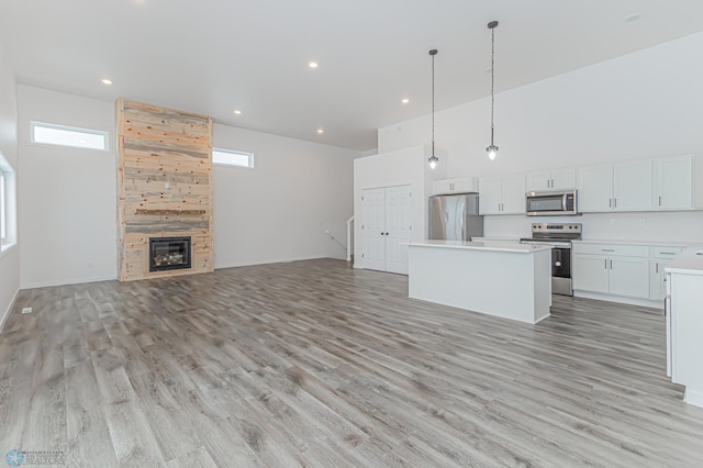 kitchen featuring a center island, decorative light fixtures, white cabinetry, stainless steel appliances, and a tile fireplace