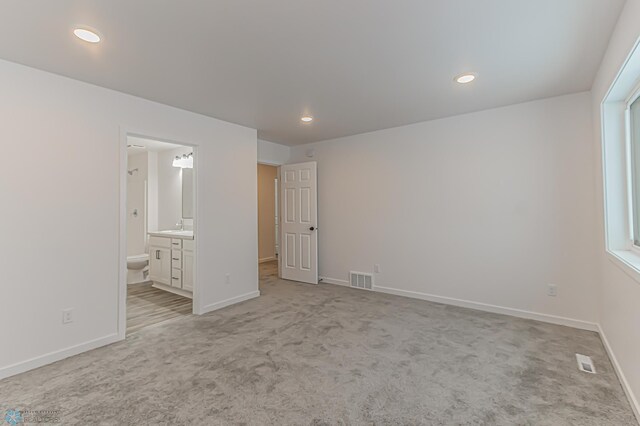 unfurnished bedroom featuring light carpet, ensuite bathroom, and sink