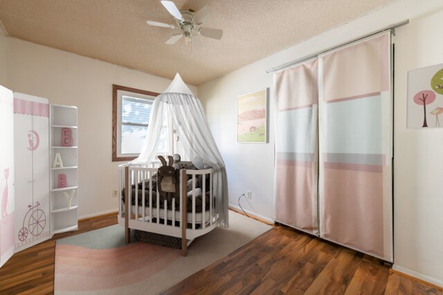 bedroom featuring ceiling fan, dark hardwood / wood-style floors, a crib, and a textured ceiling