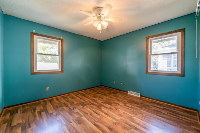 empty room with a textured ceiling, ceiling fan, hardwood / wood-style floors, and plenty of natural light