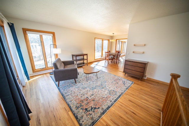 living area with a baseboard heating unit, baseboards, a textured ceiling, and light wood finished floors