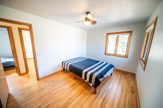 bedroom with visible vents, light wood-style flooring, a textured ceiling, and baseboards