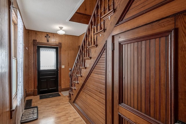 foyer featuring a textured ceiling, light hardwood / wood-style flooring, and wooden walls