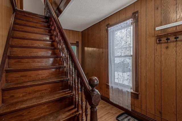 stairs with wooden walls, a textured ceiling, and hardwood / wood-style flooring