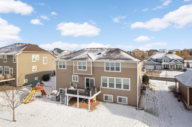 snow covered house featuring a playground and a deck