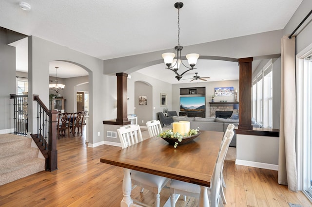 dining area with a fireplace, a textured ceiling, ceiling fan with notable chandelier, light wood-type flooring, and ornate columns