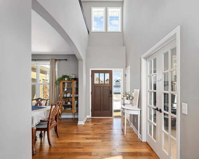 foyer entrance with arched walkways, french doors, a healthy amount of sunlight, and wood finished floors