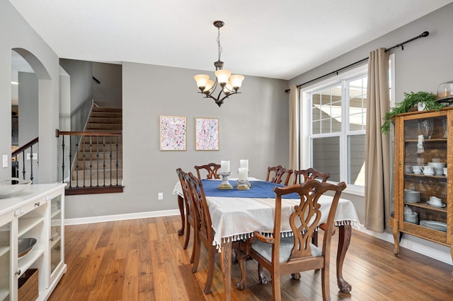 dining space featuring light wood-style floors, an inviting chandelier, baseboards, and stairs