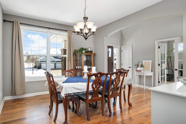 dining room featuring arched walkways, baseboards, light wood finished floors, and an inviting chandelier