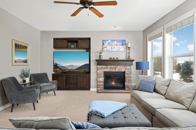 living room featuring a textured ceiling, a stone fireplace, carpet flooring, a ceiling fan, and baseboards