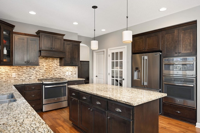 kitchen with tasteful backsplash, wood finished floors, stainless steel appliances, dark brown cabinets, and under cabinet range hood