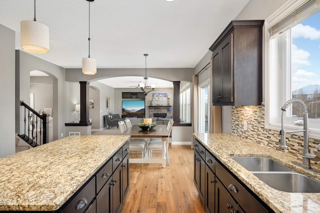 kitchen featuring arched walkways, light wood-style flooring, a sink, dark brown cabinets, and tasteful backsplash