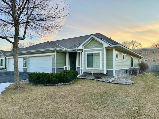 view of front of house with a garage, roof with shingles, driveway, and a front lawn