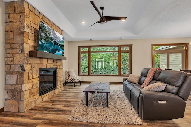 living room featuring hardwood / wood-style floors, a textured ceiling, a stone fireplace, and a raised ceiling