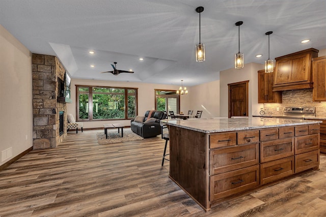 kitchen featuring dark hardwood / wood-style flooring, ceiling fan with notable chandelier, a raised ceiling, pendant lighting, and a kitchen island