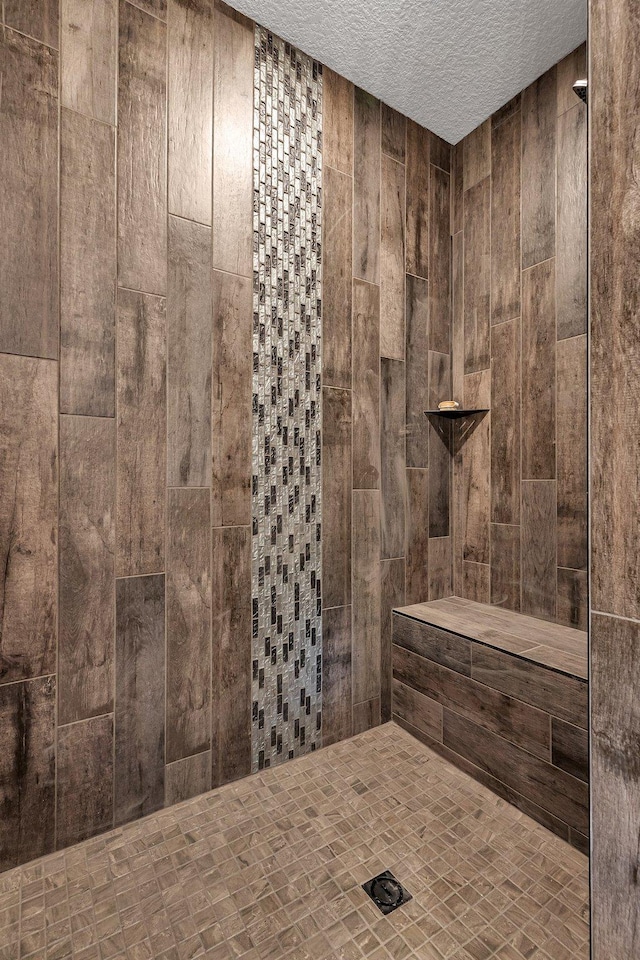 bathroom featuring tiled shower, a textured ceiling, and wooden walls