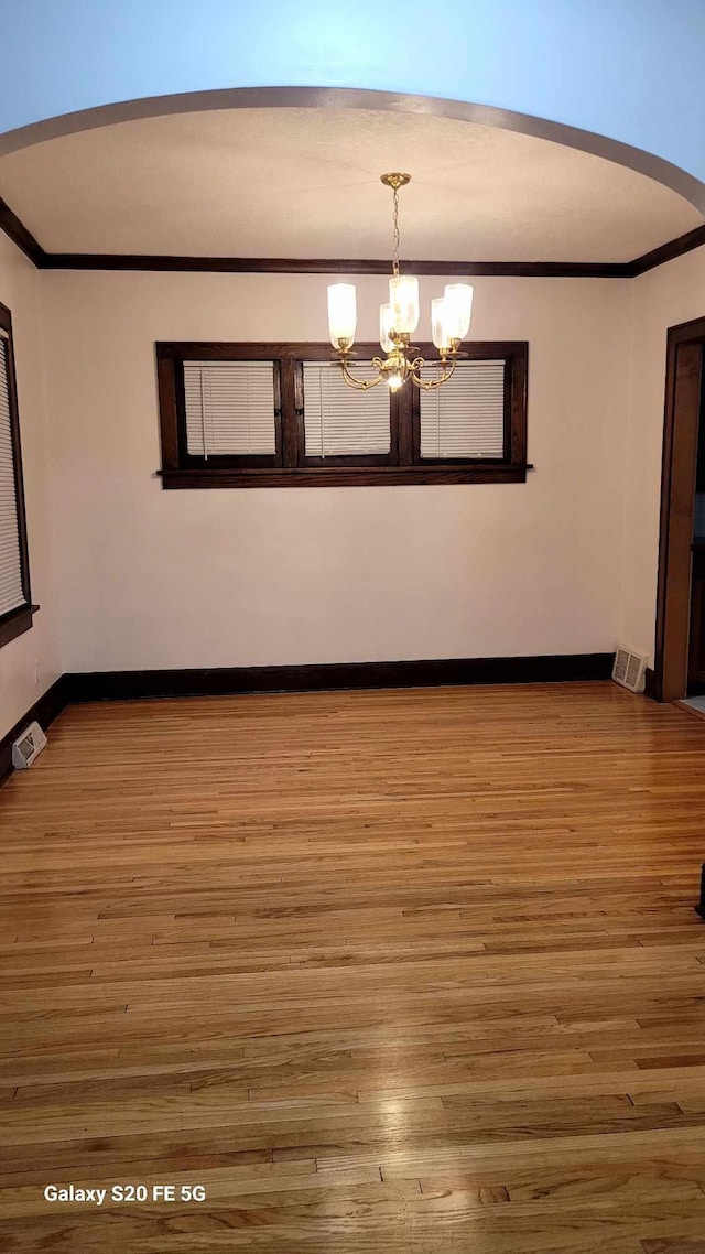 unfurnished room with wood-type flooring, ornamental molding, and an inviting chandelier