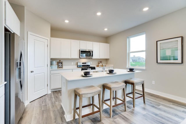 kitchen with a kitchen island with sink, white cabinets, sink, light hardwood / wood-style floors, and stainless steel appliances