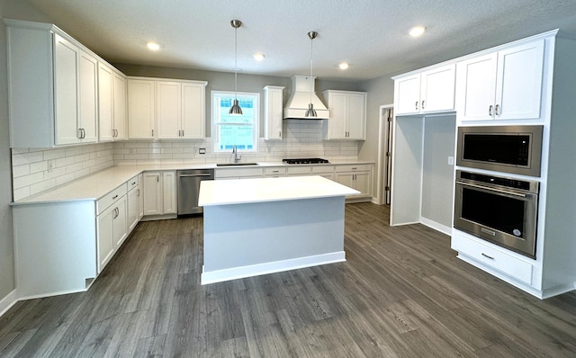 kitchen with sink, custom exhaust hood, white cabinetry, pendant lighting, and stainless steel appliances