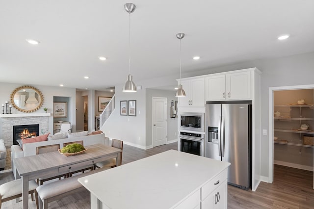 kitchen with a stone fireplace, hanging light fixtures, appliances with stainless steel finishes, a kitchen island, and white cabinets