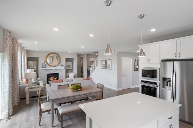 kitchen featuring stainless steel appliances, white cabinetry, a stone fireplace, and decorative light fixtures