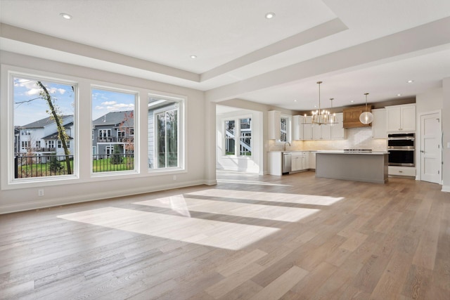 unfurnished living room featuring a raised ceiling, light hardwood / wood-style flooring, an inviting chandelier, and sink