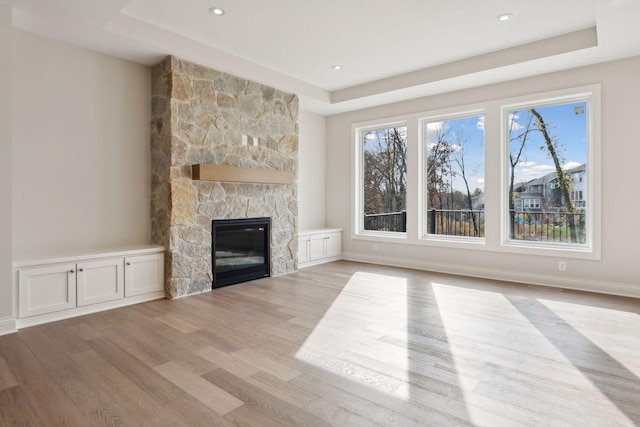 unfurnished living room with a healthy amount of sunlight, a raised ceiling, a fireplace, and light hardwood / wood-style flooring