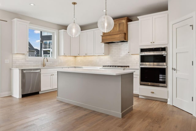 kitchen with decorative light fixtures, stainless steel appliances, white cabinetry, and a kitchen island