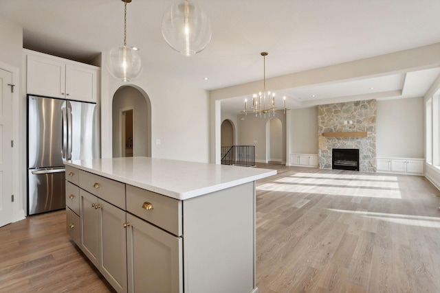 kitchen with a fireplace, stainless steel refrigerator, hanging light fixtures, and a kitchen island