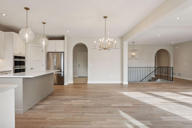 kitchen with white cabinetry, hanging light fixtures, light hardwood / wood-style flooring, a kitchen island, and appliances with stainless steel finishes