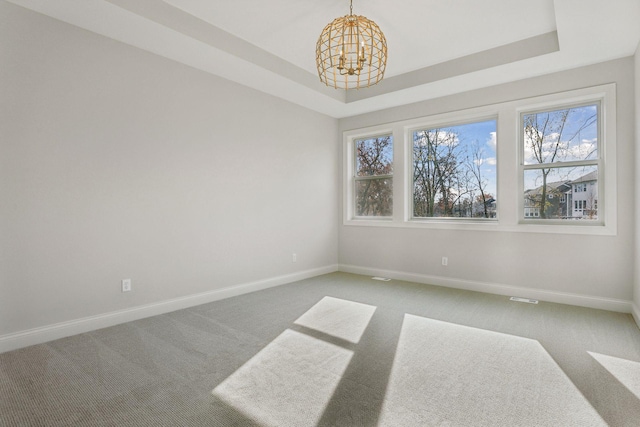 unfurnished room with a tray ceiling, carpet, and an inviting chandelier