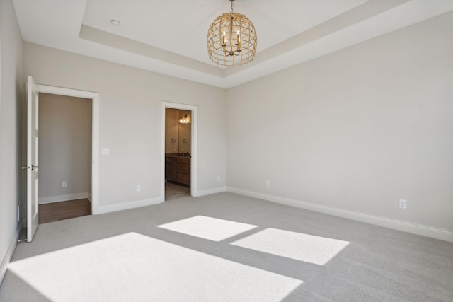 unfurnished bedroom with a raised ceiling, ensuite bath, light colored carpet, and an inviting chandelier