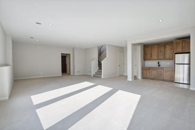 unfurnished living room featuring light carpet and sink