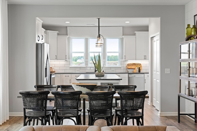 kitchen featuring backsplash, stainless steel appliances, decorative light fixtures, white cabinets, and light hardwood / wood-style floors