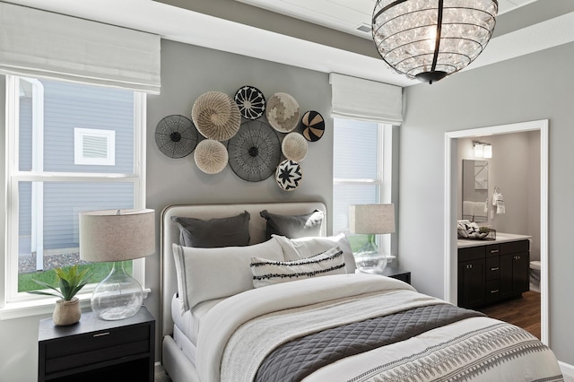 bedroom with a notable chandelier, ensuite bathroom, dark hardwood / wood-style flooring, and multiple windows