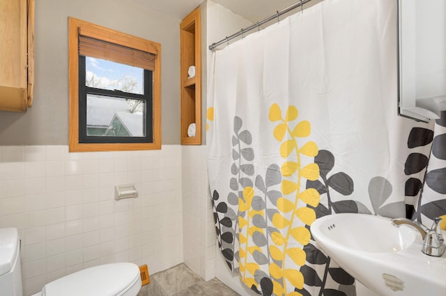 full bath with toilet, a wainscoted wall, a shower with shower curtain, a sink, and tile walls