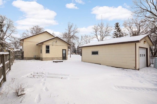 snow covered property featuring a detached garage, fence, and an outbuilding