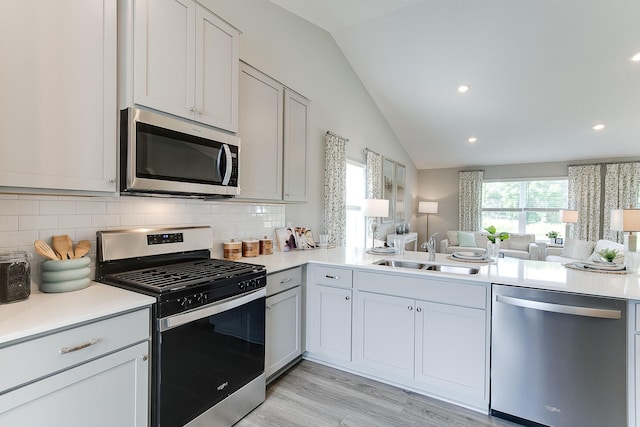 kitchen featuring appliances with stainless steel finishes, backsplash, sink, light hardwood / wood-style flooring, and lofted ceiling