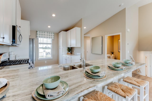 kitchen featuring stainless steel appliances, light stone counters, white cabinetry, and sink