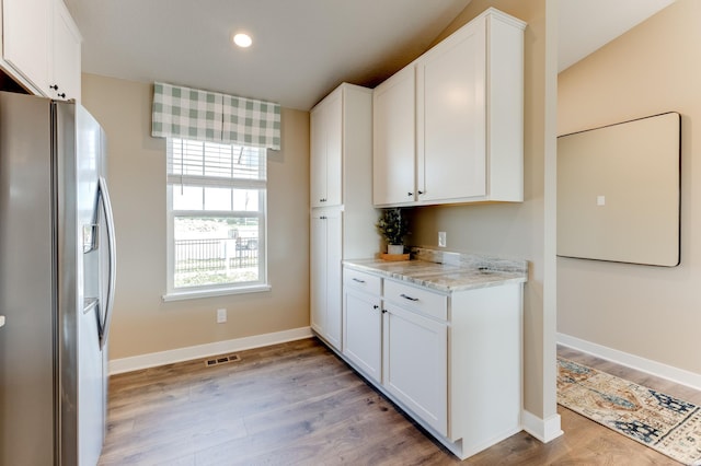 kitchen featuring white cabinetry, stainless steel fridge with ice dispenser, light hardwood / wood-style floors, and light stone counters