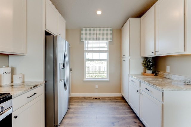 kitchen with light stone countertops, white cabinets, light hardwood / wood-style floors, and appliances with stainless steel finishes