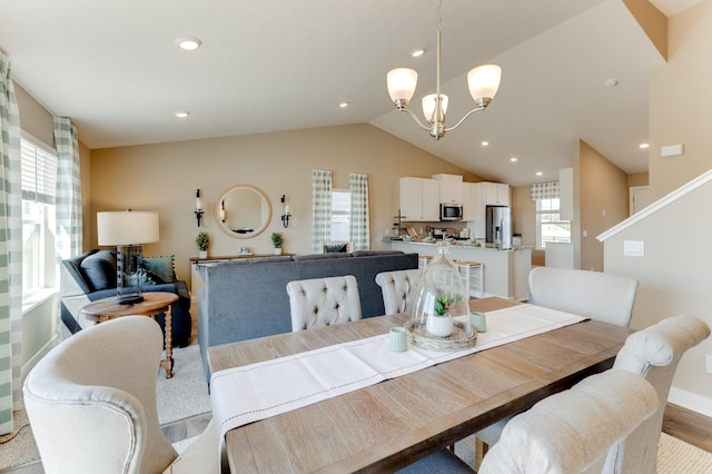 dining area with light wood-type flooring, vaulted ceiling, and an inviting chandelier