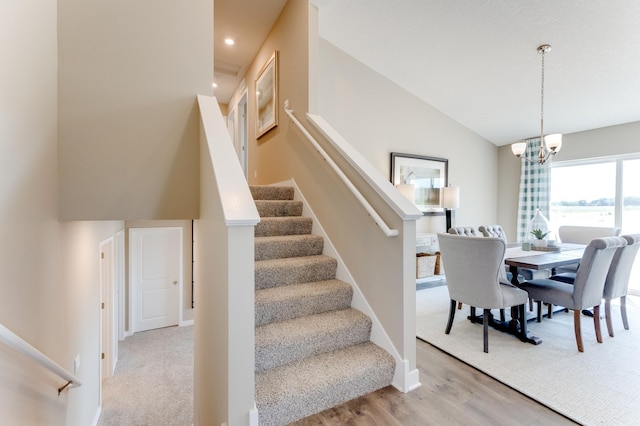 stairway with hardwood / wood-style flooring, an inviting chandelier, and lofted ceiling