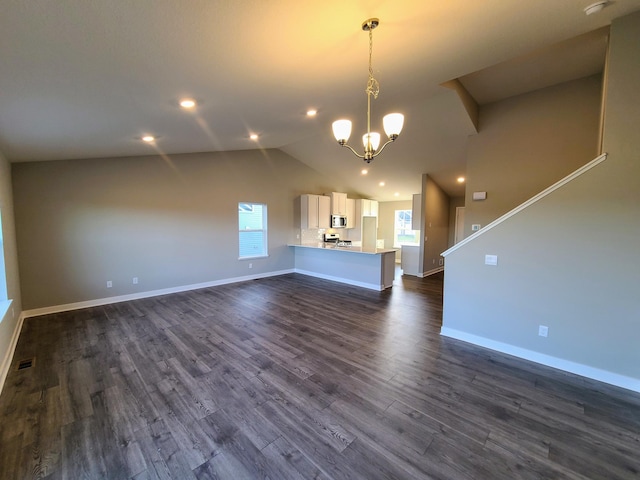 unfurnished living room with dark hardwood / wood-style flooring, an inviting chandelier, a wealth of natural light, and lofted ceiling